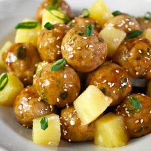 A side view of a plate of teriyaki pineapple chicken meatballs with cubed pineapple.