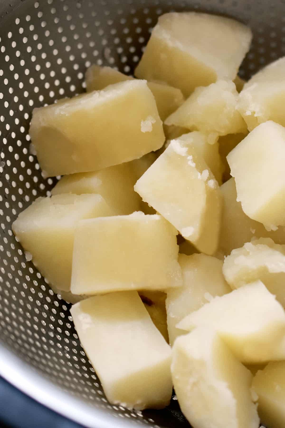 Boiled russet potato cubes in a colander.