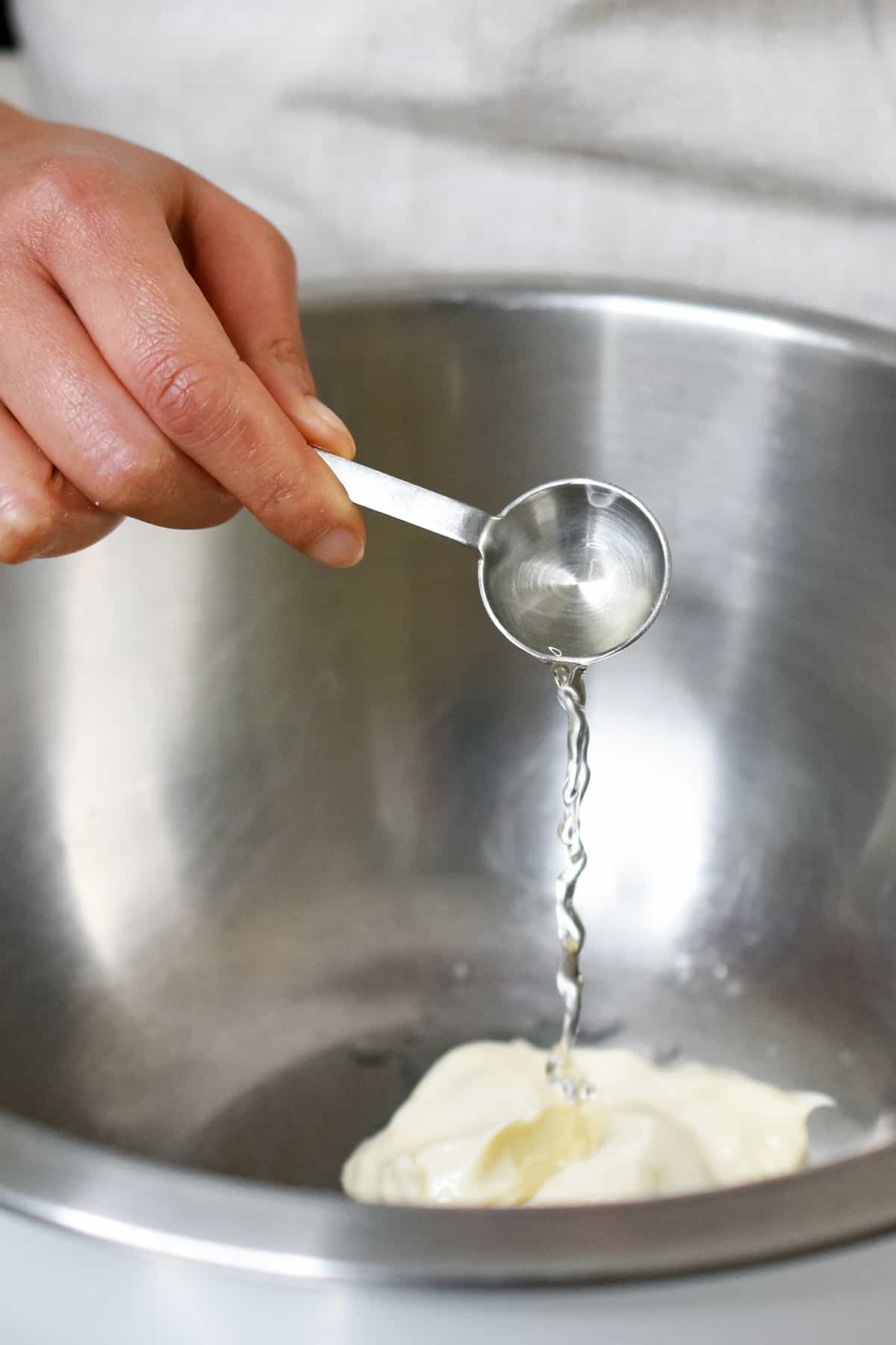 Adding a spoonful of rice vinegar into a mixing bowl with a dollop of mayonnaise.