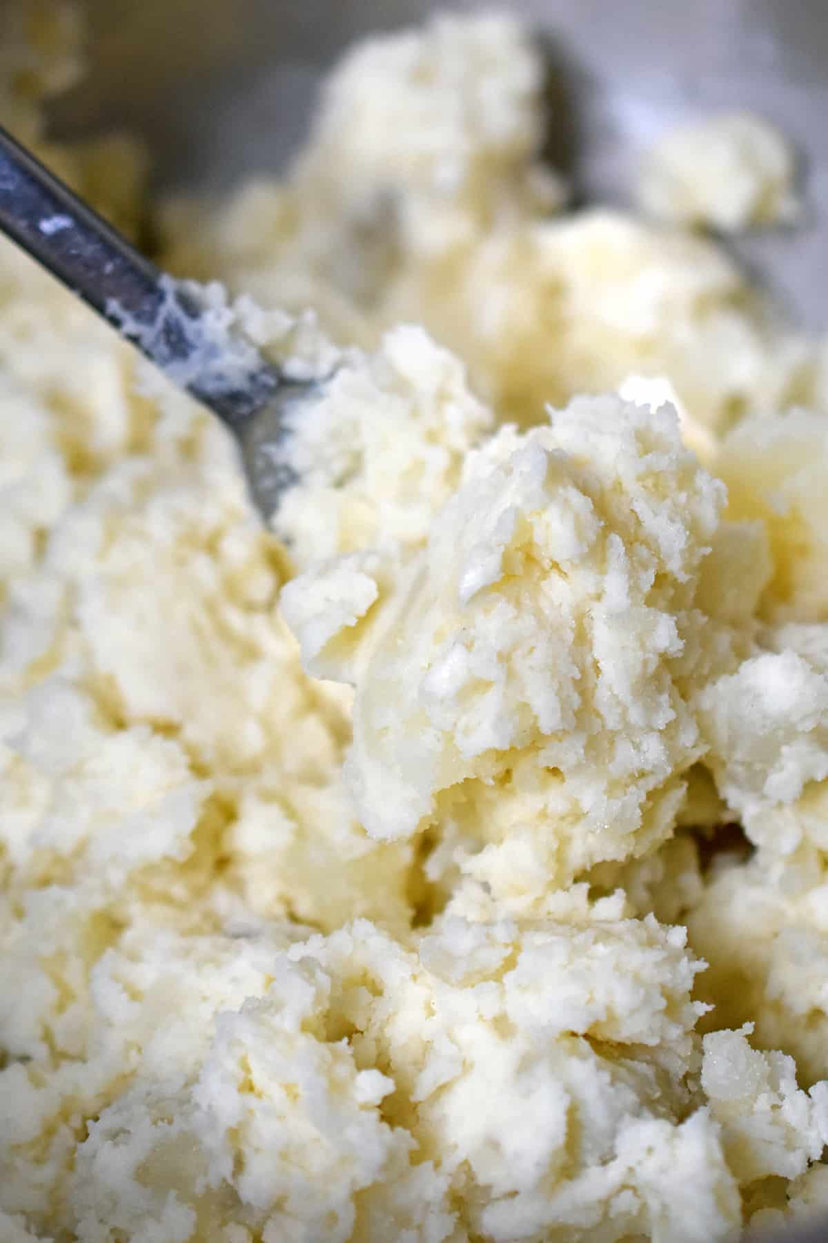 A closeup of mashed russet potatoes and seasoned mayonnaise to make Japanese potato salad.