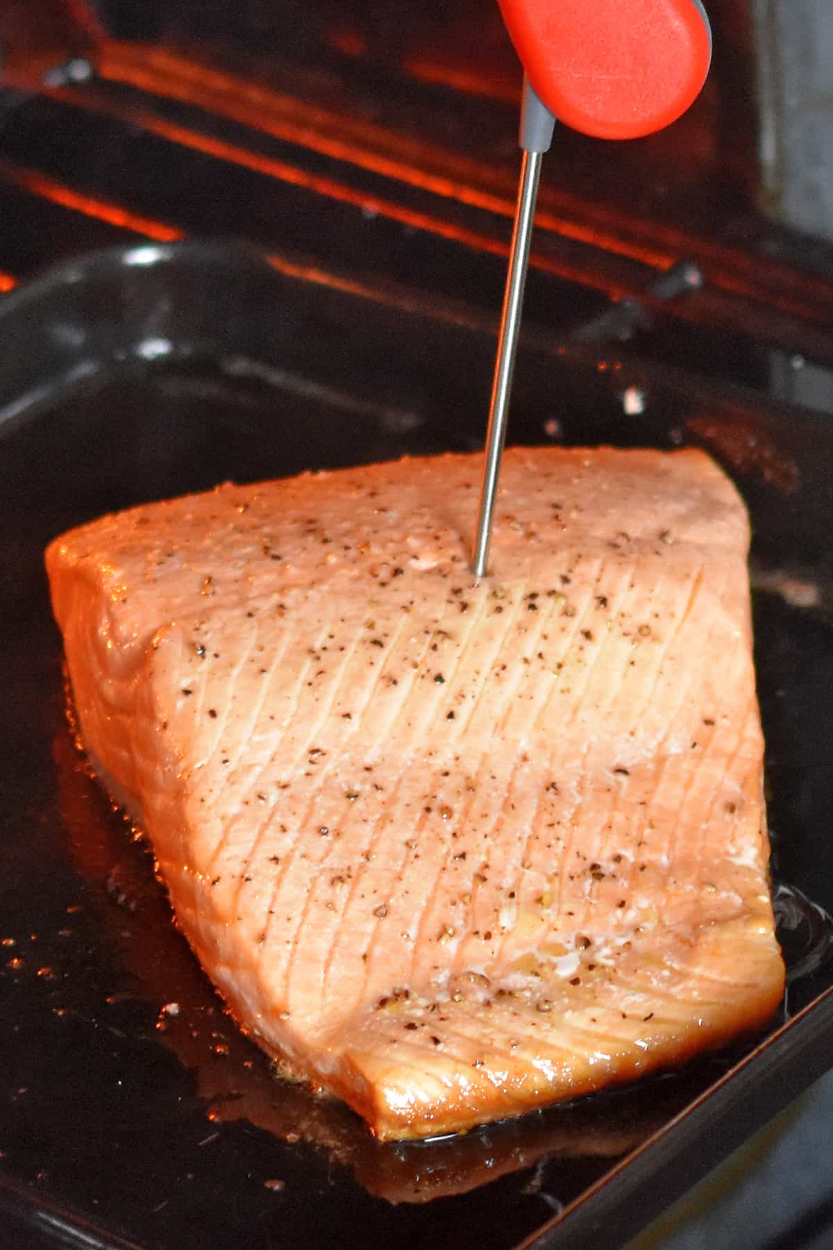 An instant read meat thermometer is inserted into a cooked salmon fillet.