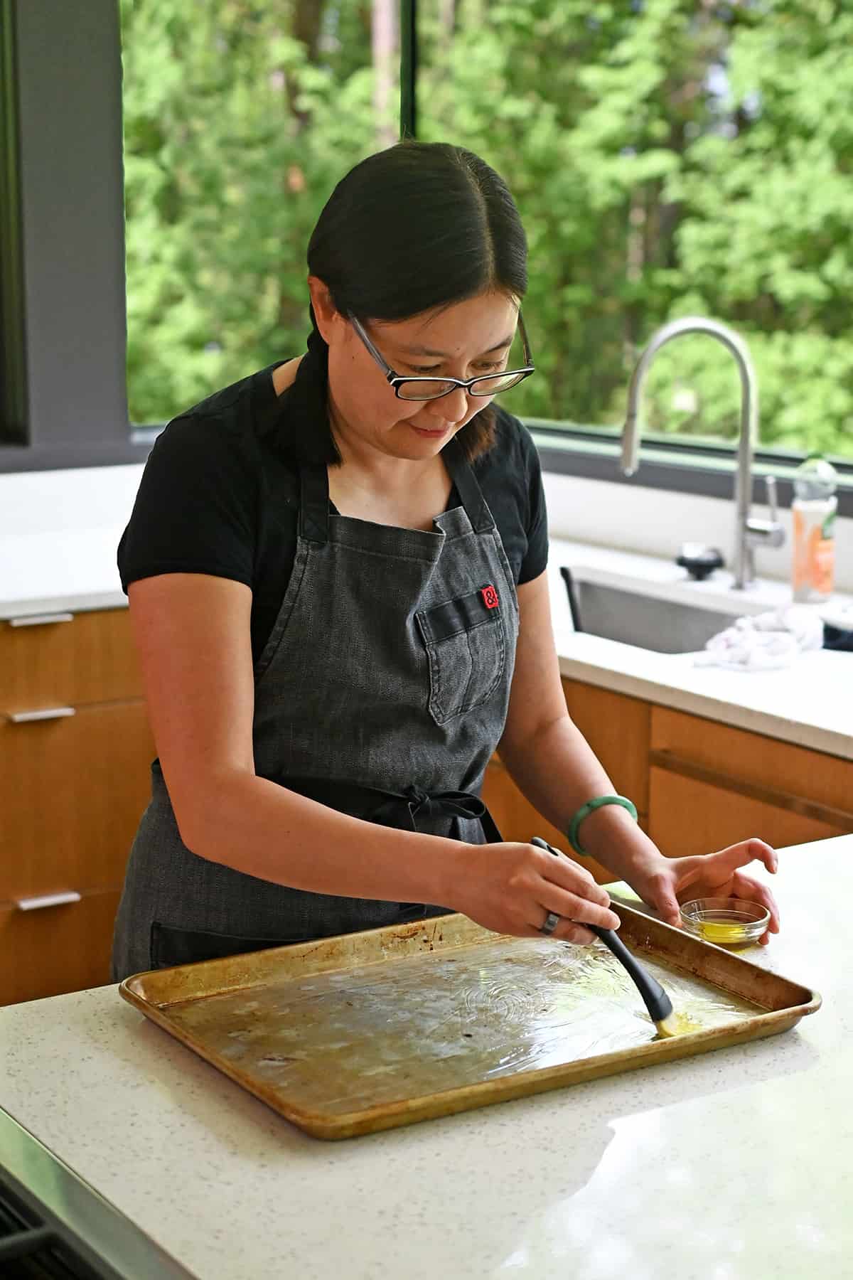 An Asian woman is brushing a sheet pan with some avocado oil.