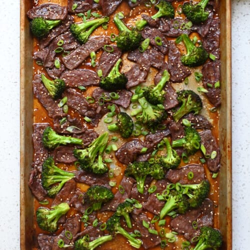 An overhead shot of sheet pan broccoli and beef topped with sliced green onions and toasted sesame seeds.
