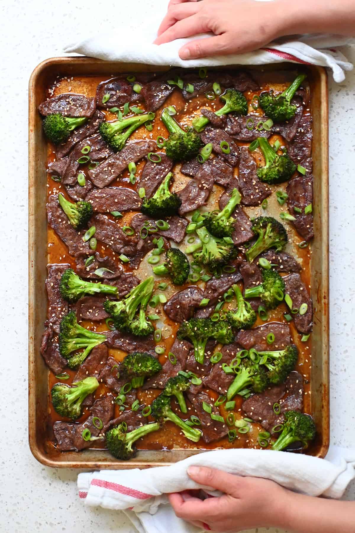 An overhead shot of sheet pan broccoli and beef topped with sliced green onions and toasted sesame seeds.