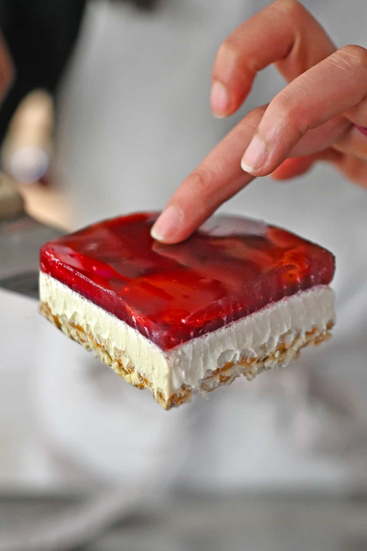 A slice of grain-free, refined sugar free, and dairy-free strawberry pretzel salad is being lifted up with a spatula.