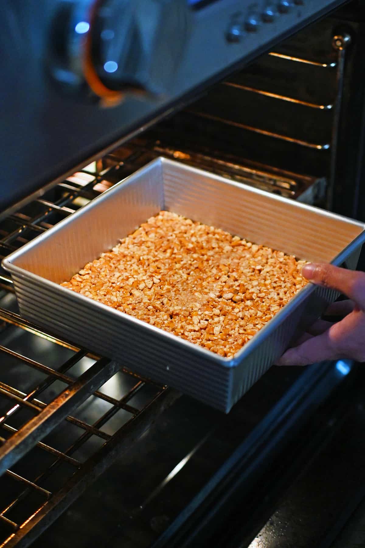 A square baking pan with a gluten-free pretzel crust is being placed into an open oven.