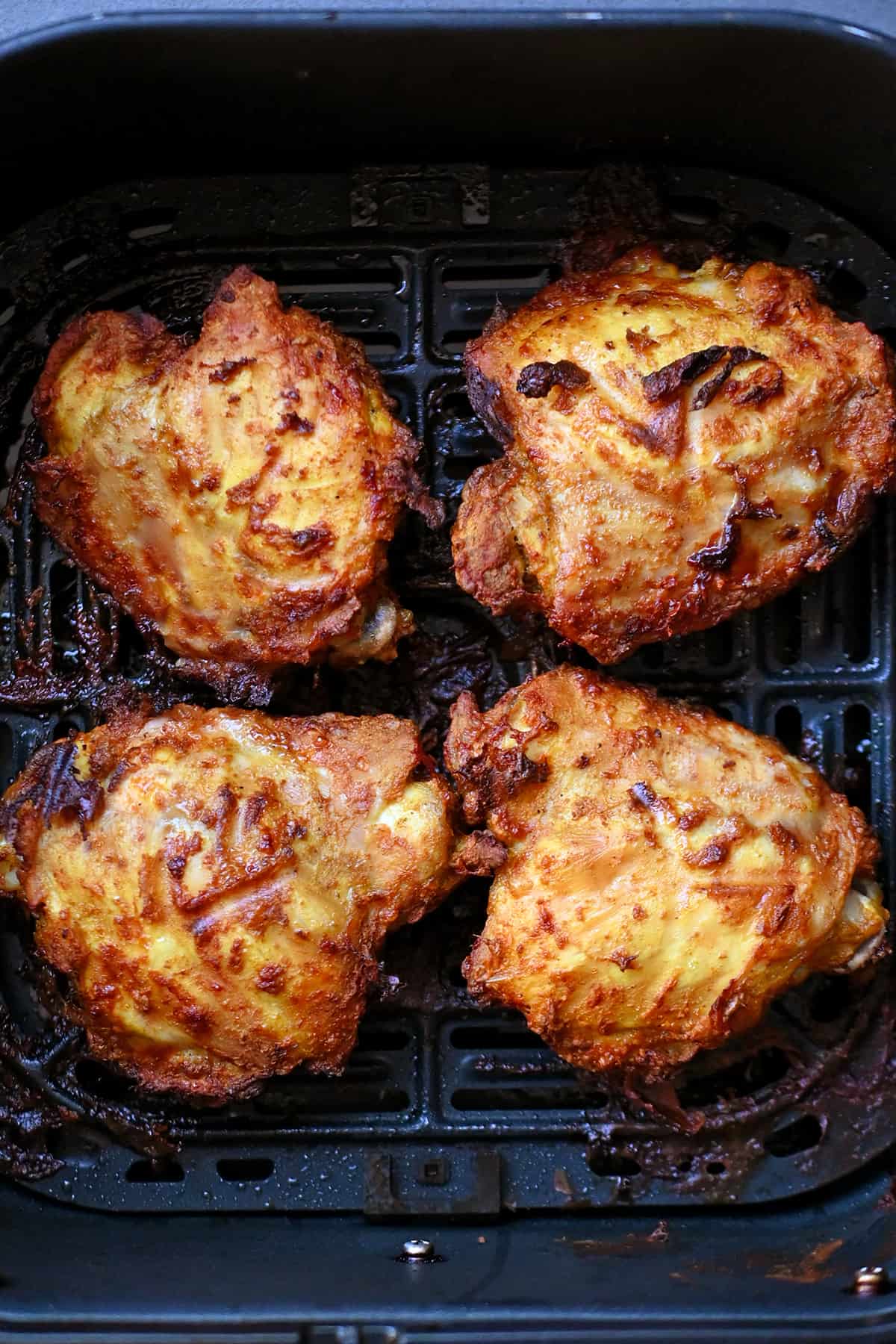 An air fryer filled with four golden brown tandoori chicken thighs.