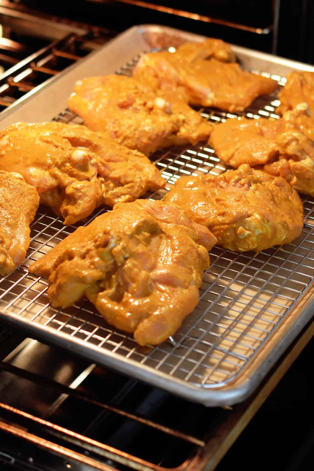 A tray of tandoori chicken is placed in an open oven.