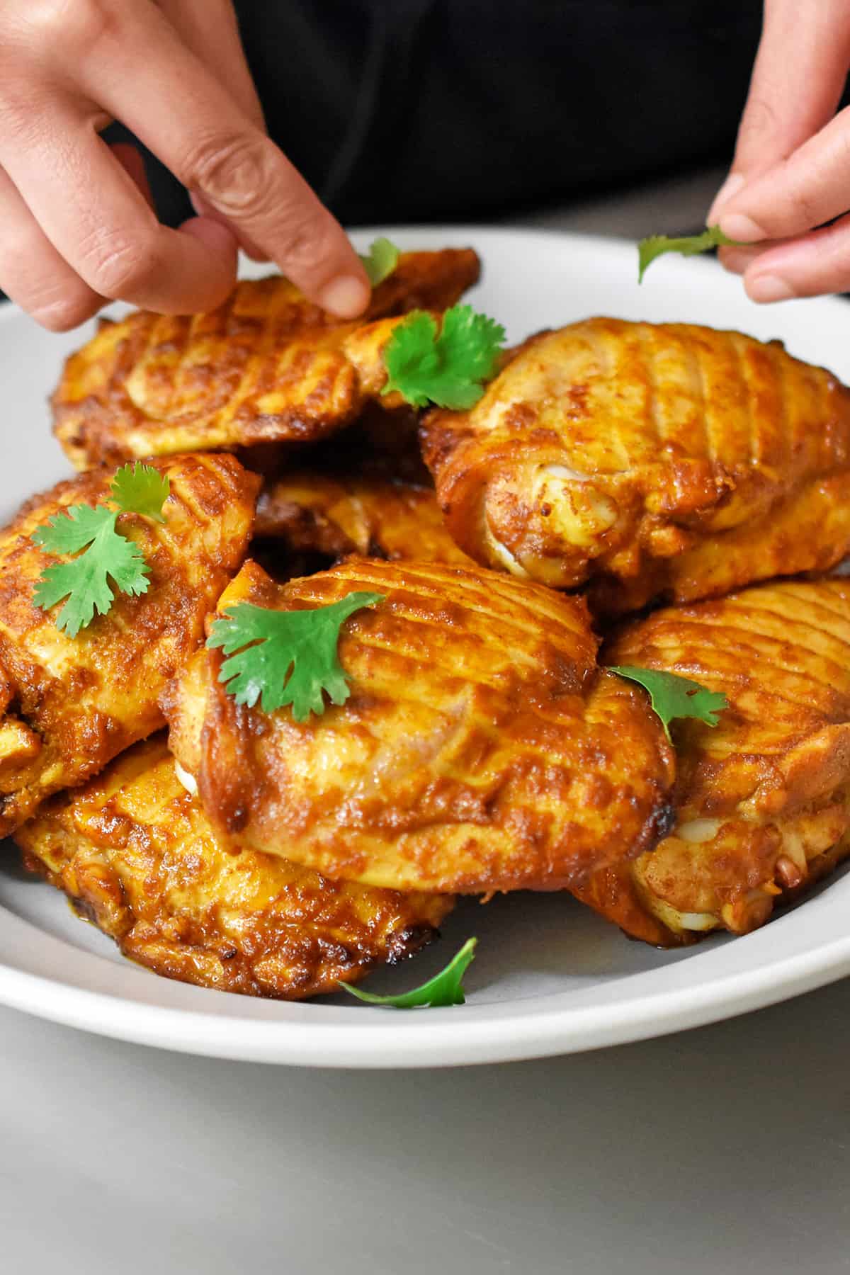 A hand is adding cilantro leaves to a platter of tandoori chicken.