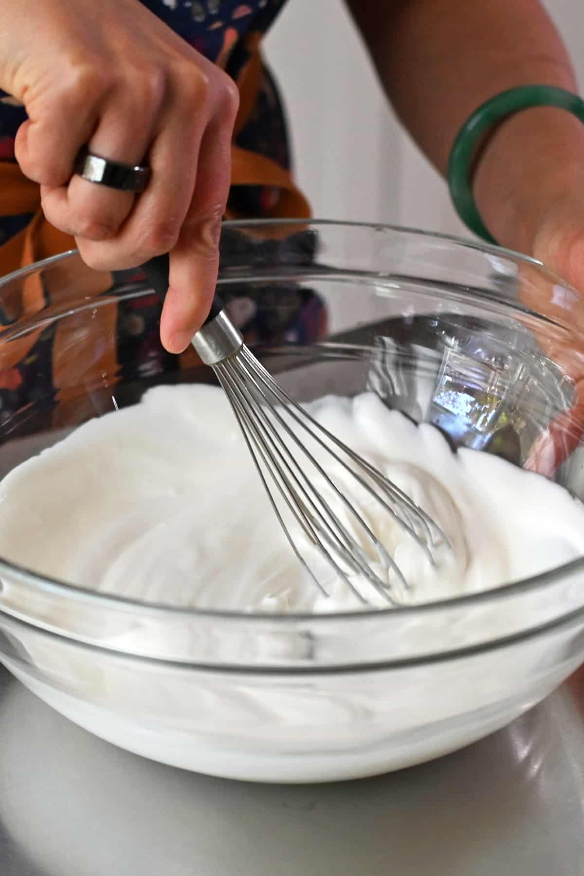 A whisk is mixing a creamy coconut yogurt base for paleo ambrosia in a glass mixing bowl.