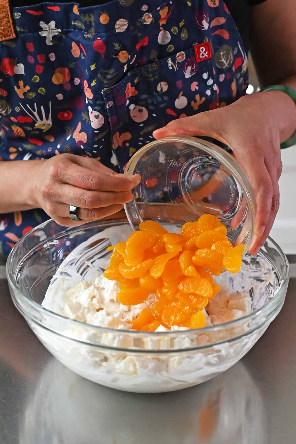 Adding a bowl of drained canned mandarin oranges into a bowl of paleo ambrosia.
