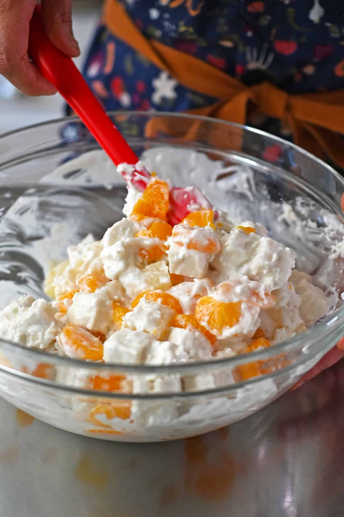 Mixing ambrosia salad in a large glas bowl with a red silicone spatula.
