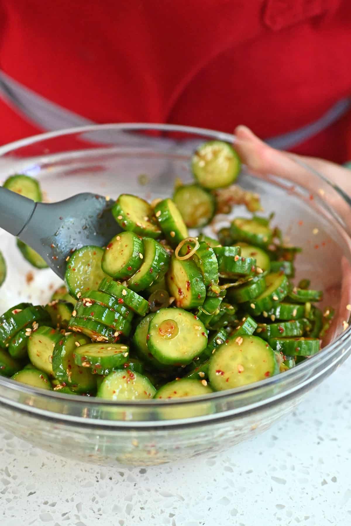 Tossing Korean cucumber salad with a gray silicone spatula in a glass bowl.