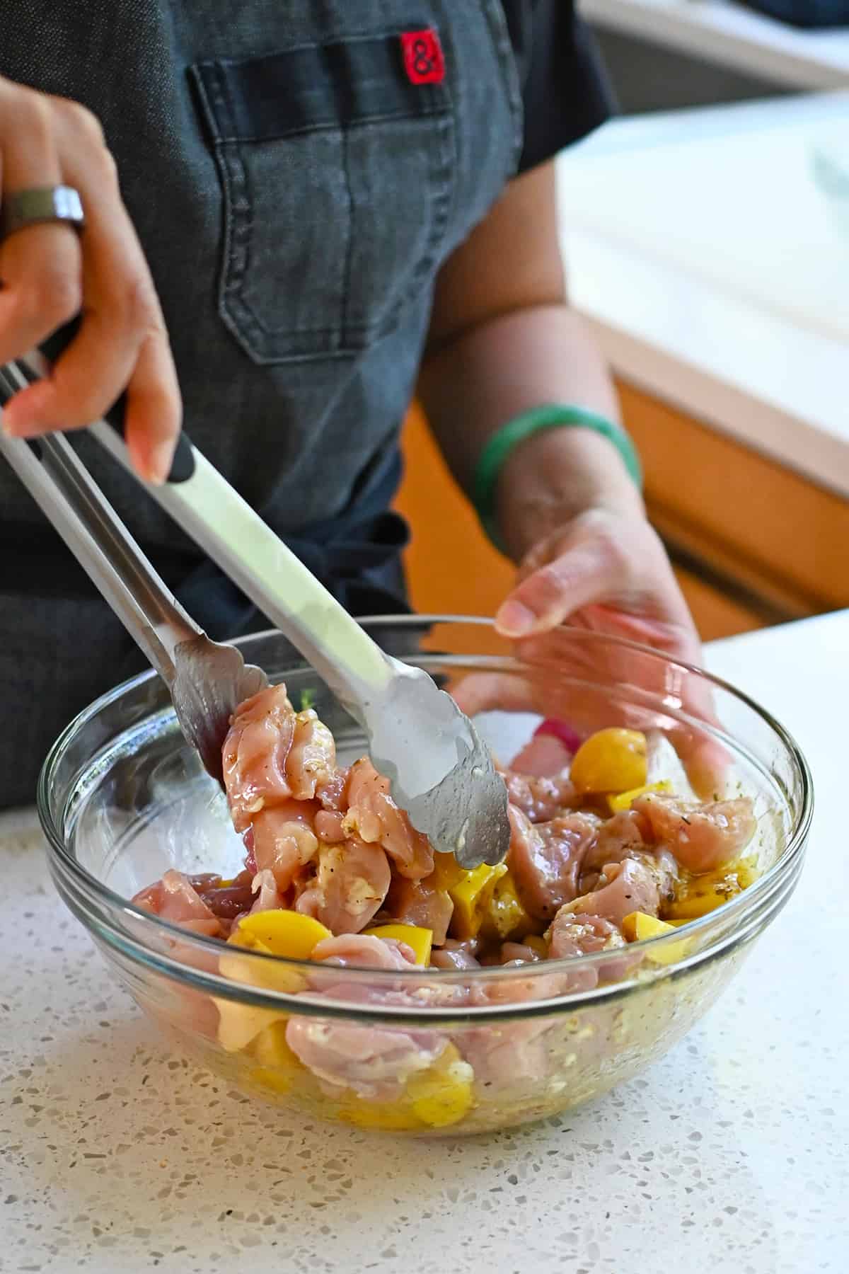 Tossing raw chicken thigh cubes and cut up yellow potatoes in a bowl with a Greek marinade.