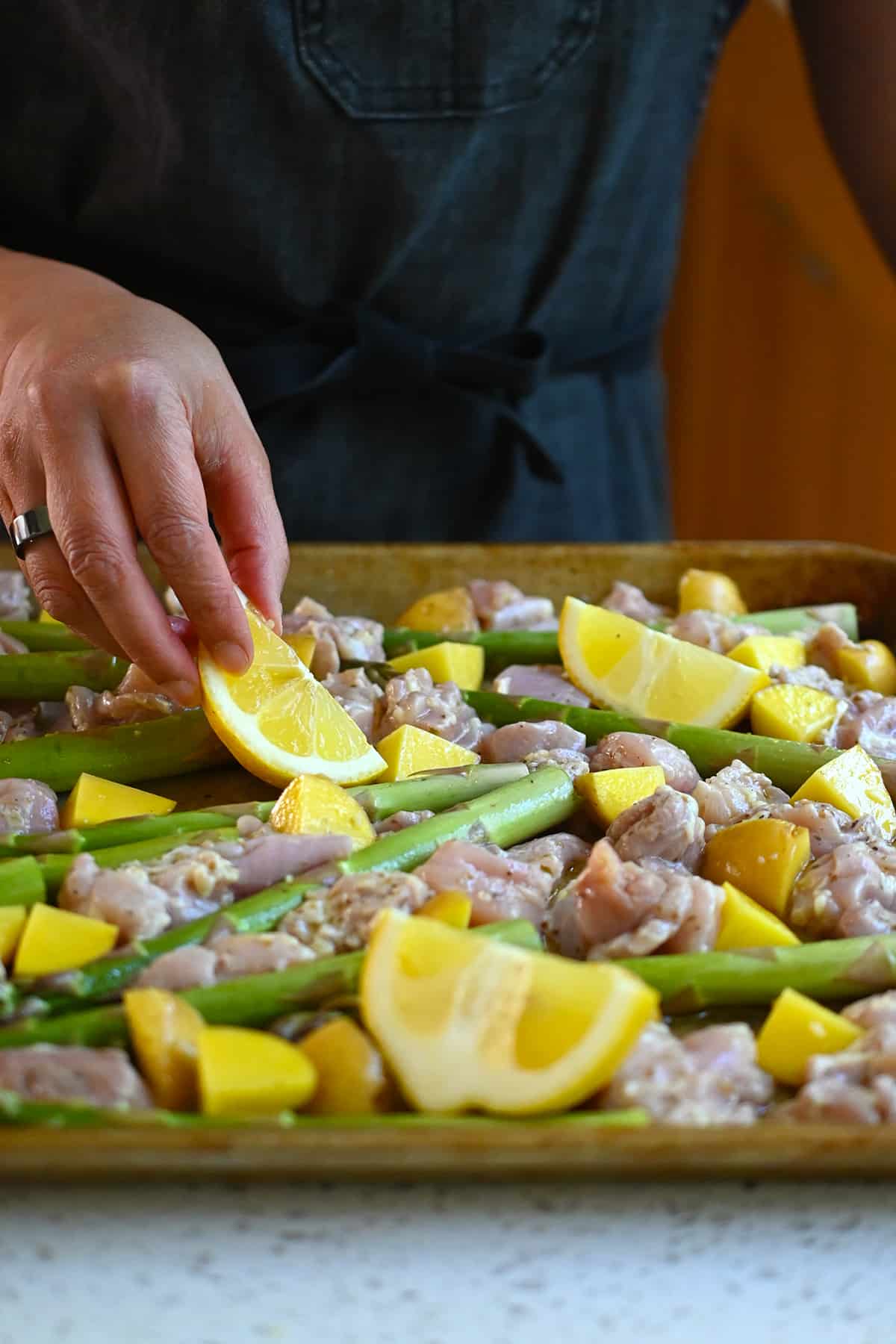 Adding lemon wedges to a sheet pan with chicken, asparagus, and potatoes.