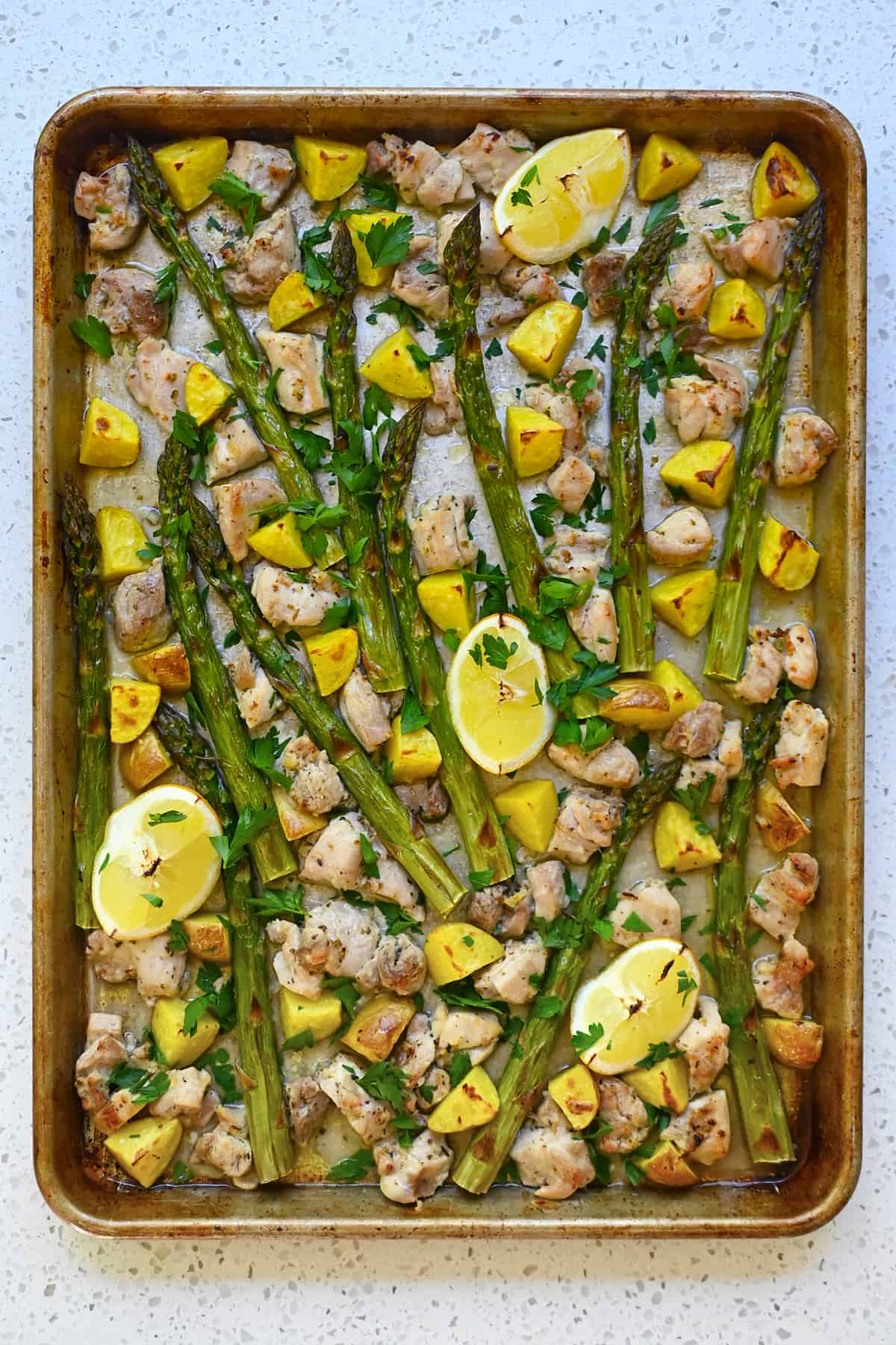 An overhead shot of Greek sheet pan chicken with asparagus, chicken, and potatoes topped with Italian parsley.