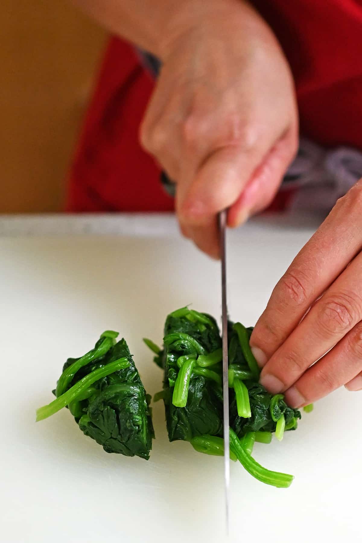 Cutting cooked and squeezed dry spinach into three sections with a chef's knife.