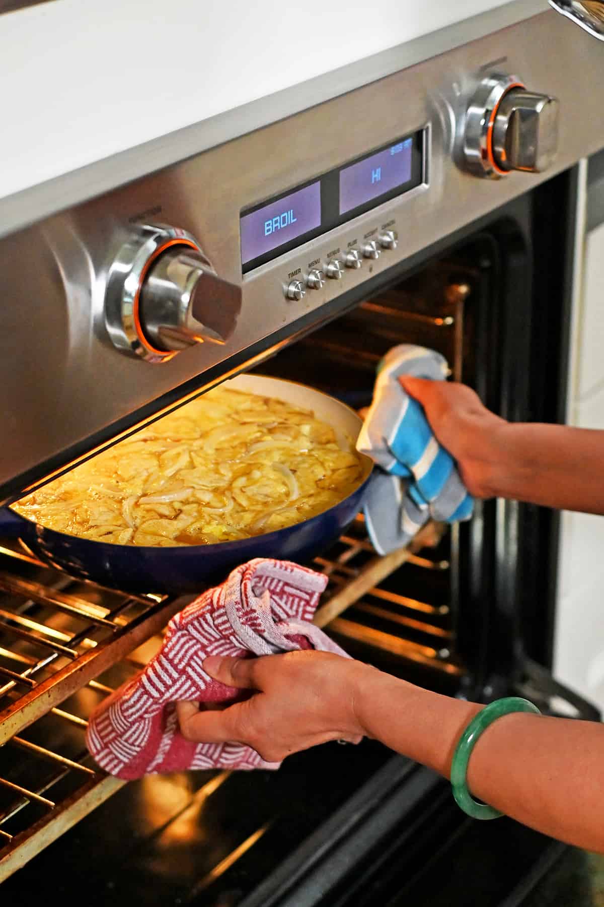 Two hands are placing a blue skillet filled with Spanish tortilla made with potato chips into an oven set on broil.