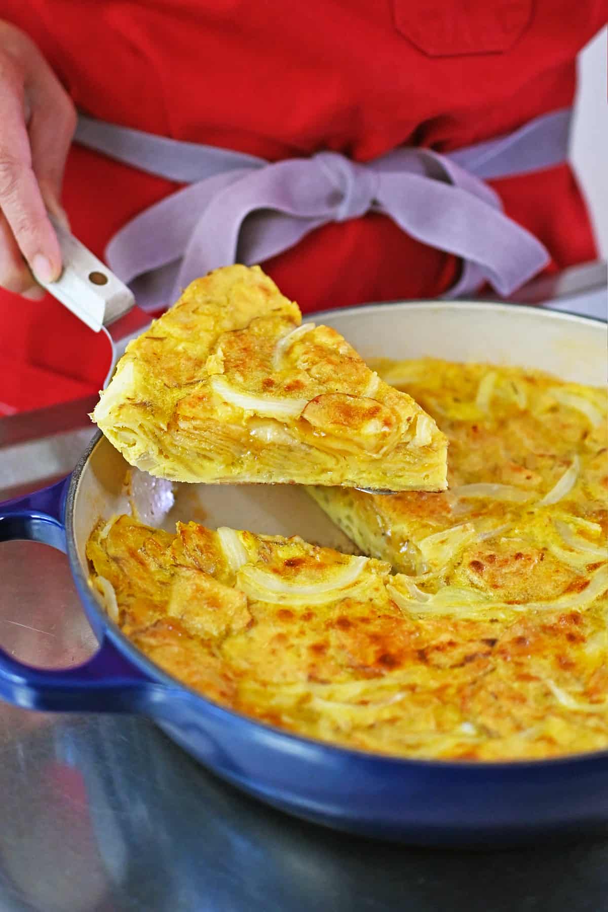 Lifting up a slice of Spanish tortilla made with potato chips from a blue skillet.