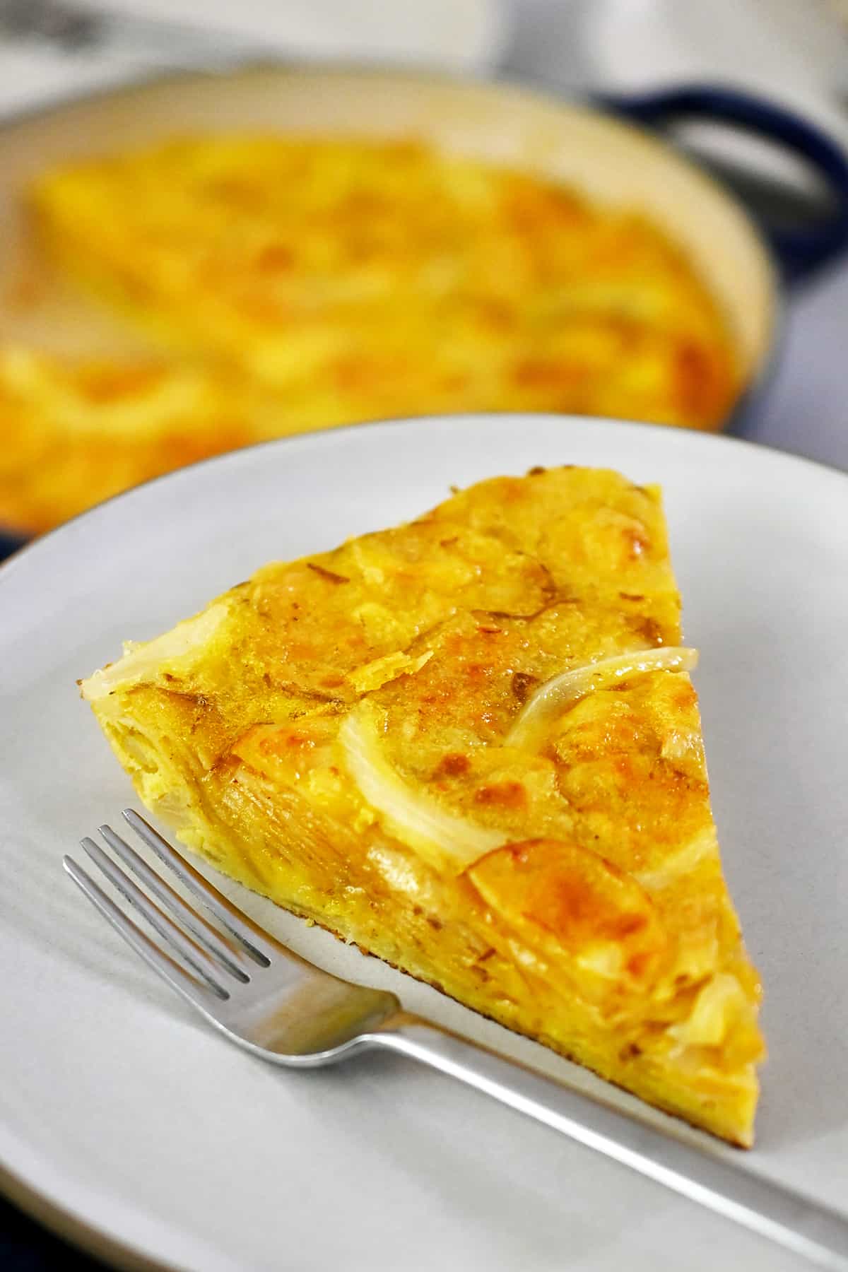 A slice of Spanish tortilla made with potato chips on a white plate next to a fork.