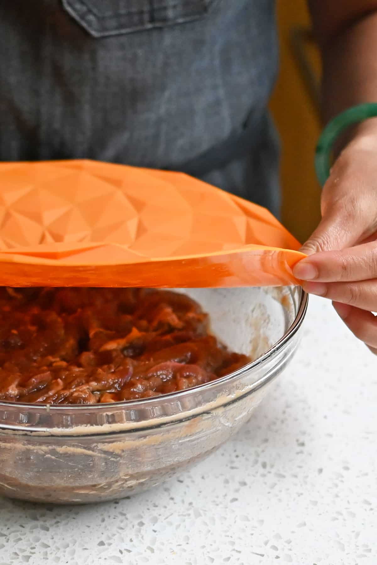 Placing an orange silicone lid on top of a bowl filled with marinated bulgogi beef.