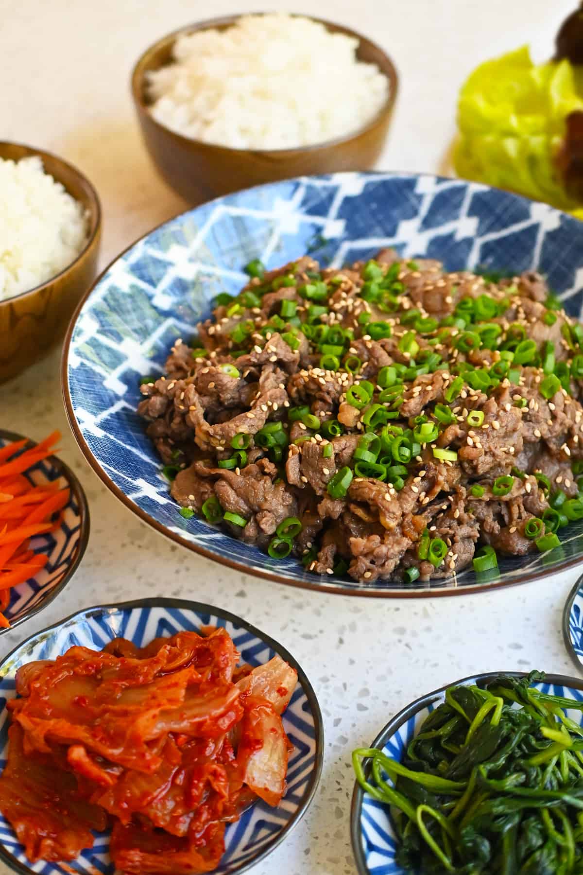 A bowl of paleo and gluten free bulgogi surrounded by small bowls of banchan and steamed white rice.