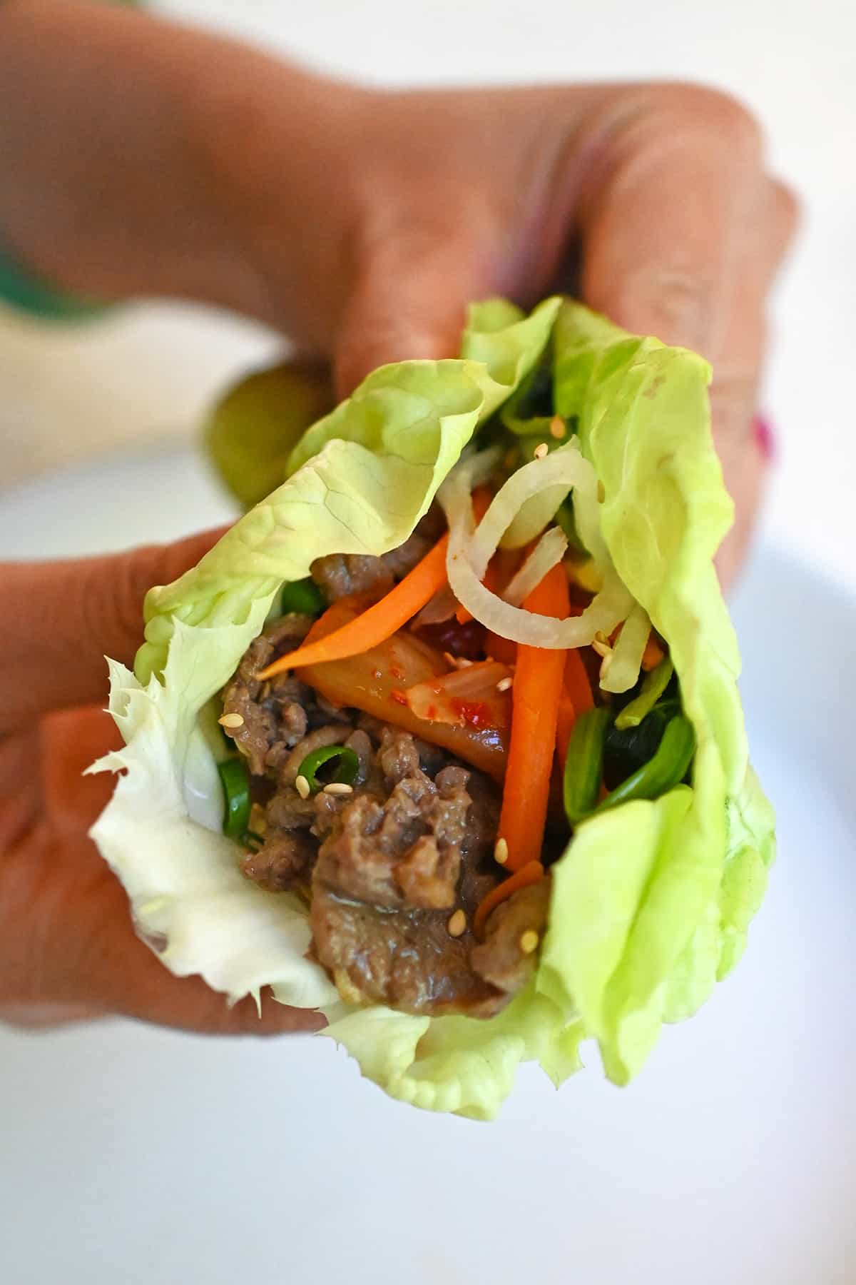 A closeup of a hand holding bulgogi and vegetables wrapped in a lettuce leaf.