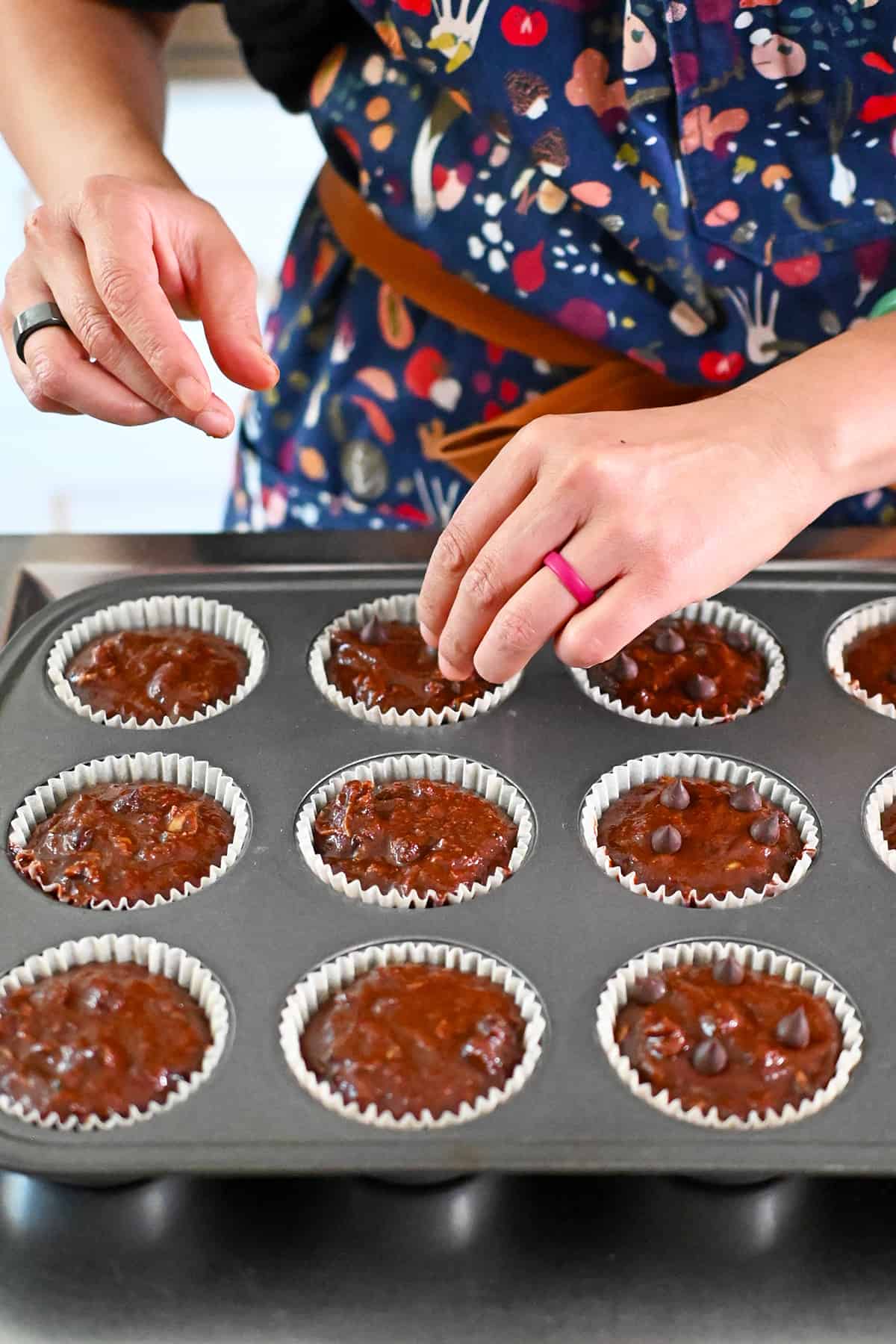 Adding extra chocolate chips on top of chocolate zucchini muffins before baking them in the oven.