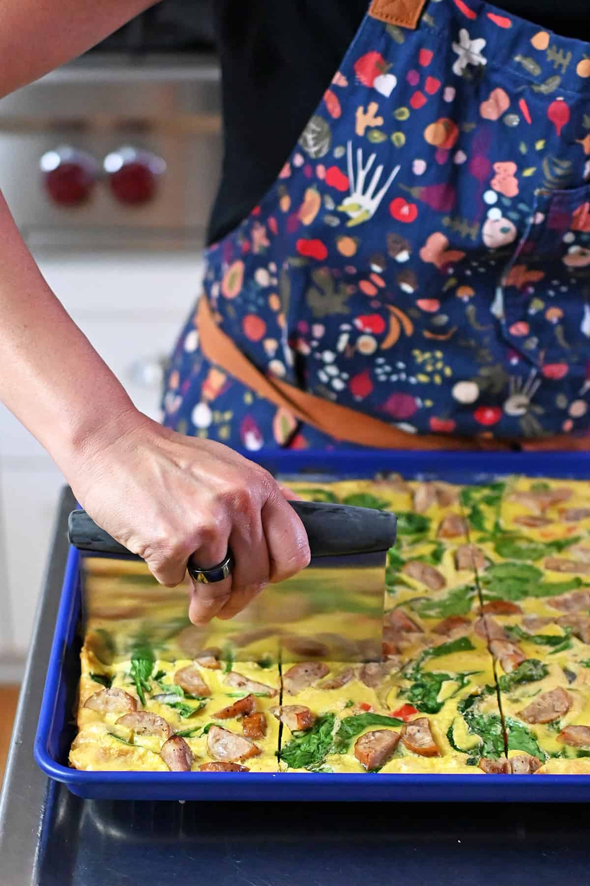 Slicing cooked sheet pan eggs with a metal dough scraper.