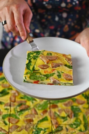 A square slice of sheet pan eggs on a small plate over a pan of sheet pan eggs.