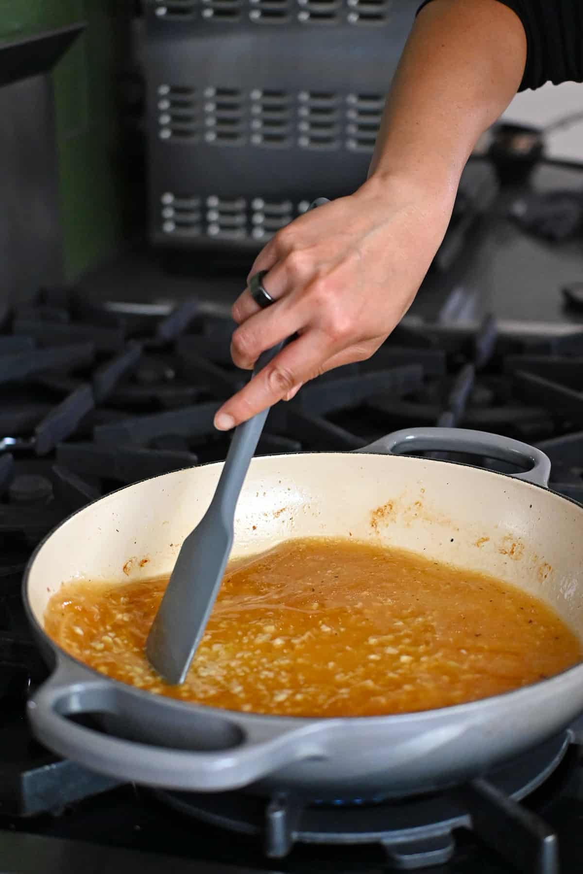 A gray silicone spatula is scraping up the fond in a pan to make lemon garlic chicken sauce.