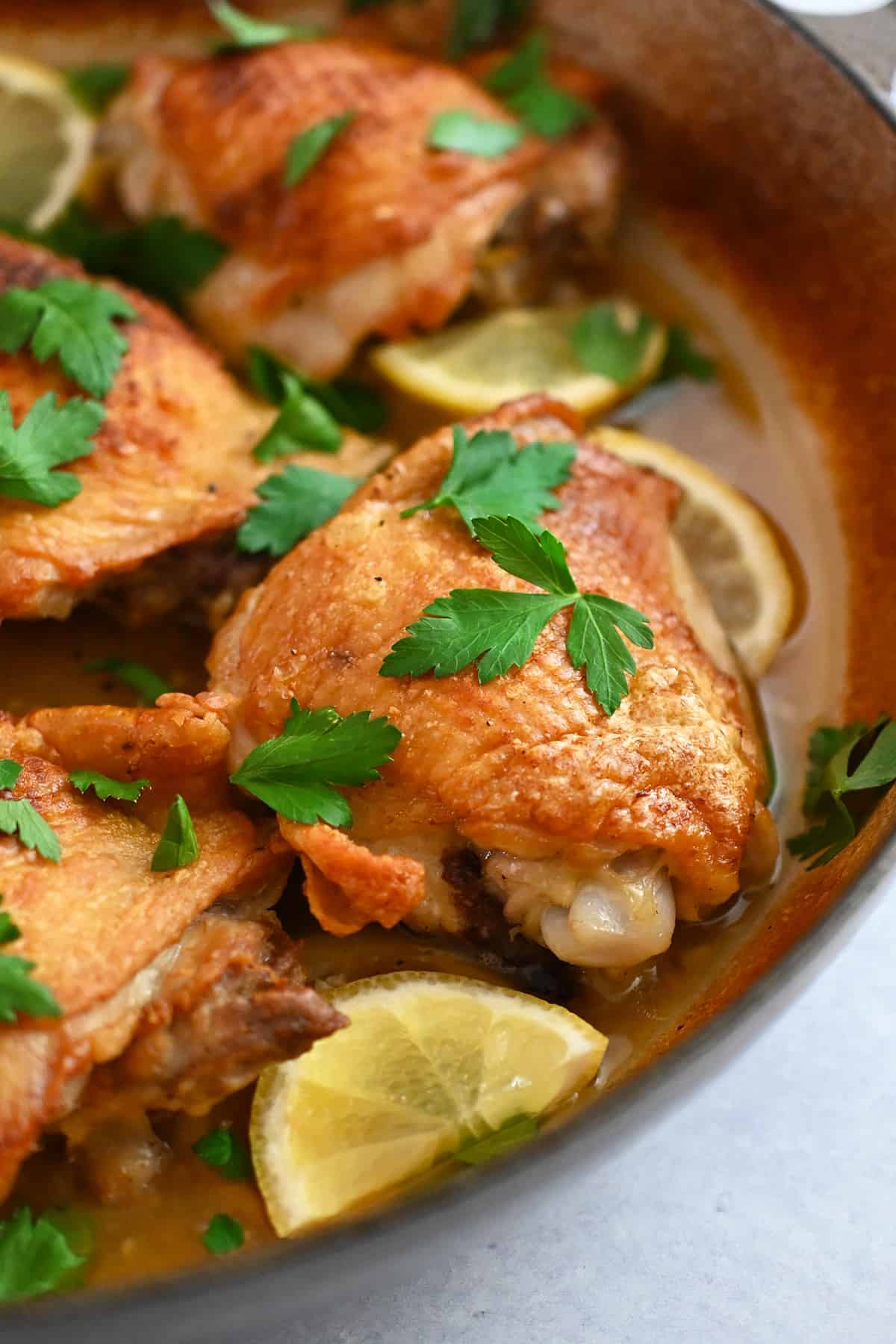 A closeup view of lemon garlic chicken thighs in a skillet with golden brown skin.