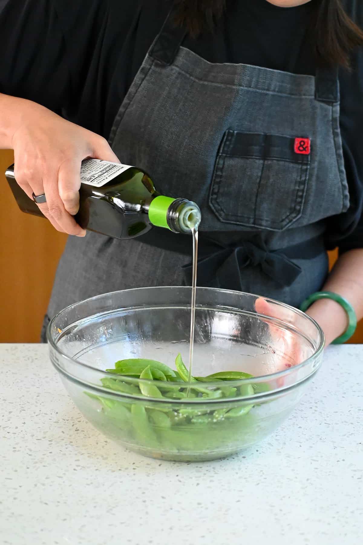Pouring avocado oil from the bottle into a bowl filled with raw sugar snap peas.