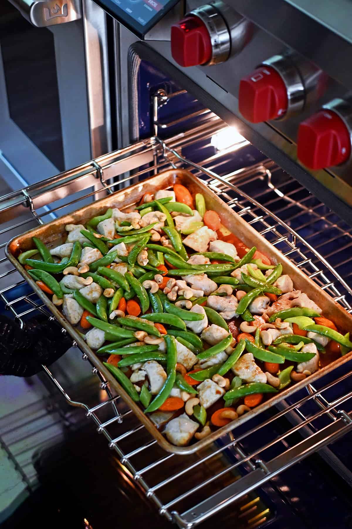 Placing a sheet pan filled with cashew chicken ingredients back into the oven to broil for a few minutes.
