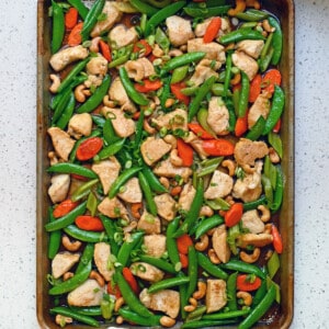 An overhead view of a two hands holding a pan of Sheet Pan Cashew Chicken.