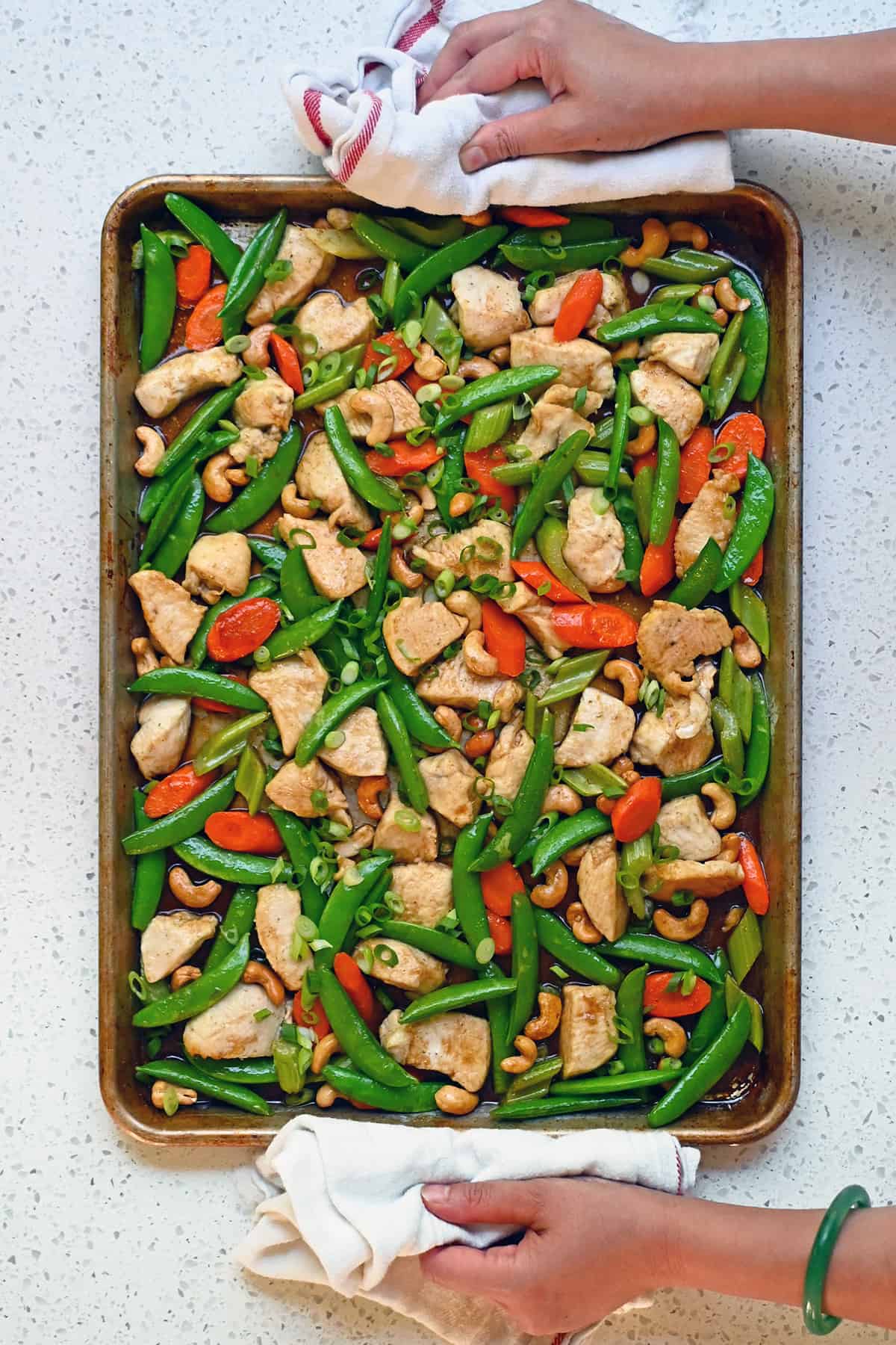 An overhead view of a two hands holding a pan of Sheet Pan Cashew Chicken.