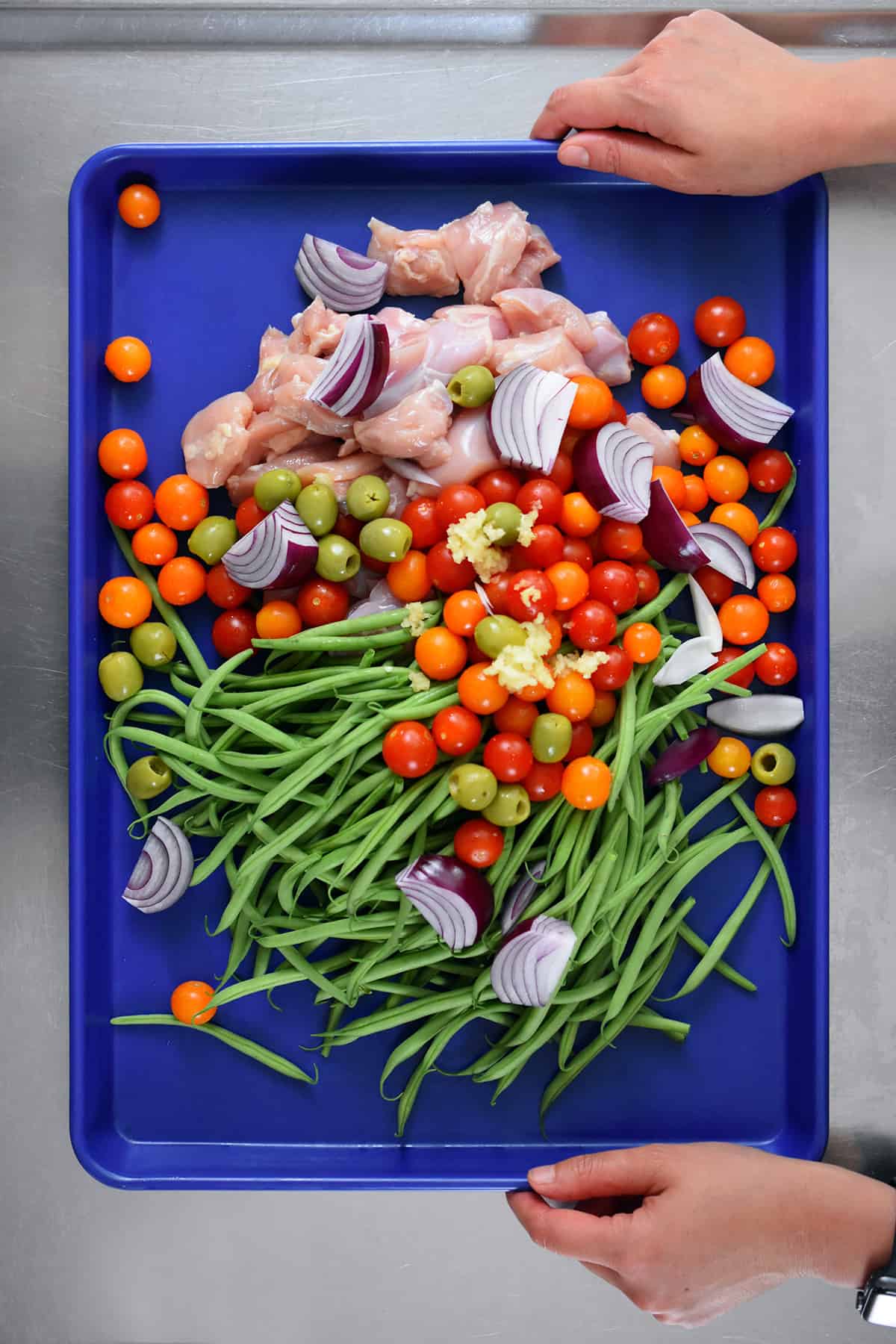 An overhead shot of the raw and unseasoned ingredients for sheet pan Italian chicken on a blue rimmmed baking sheet.