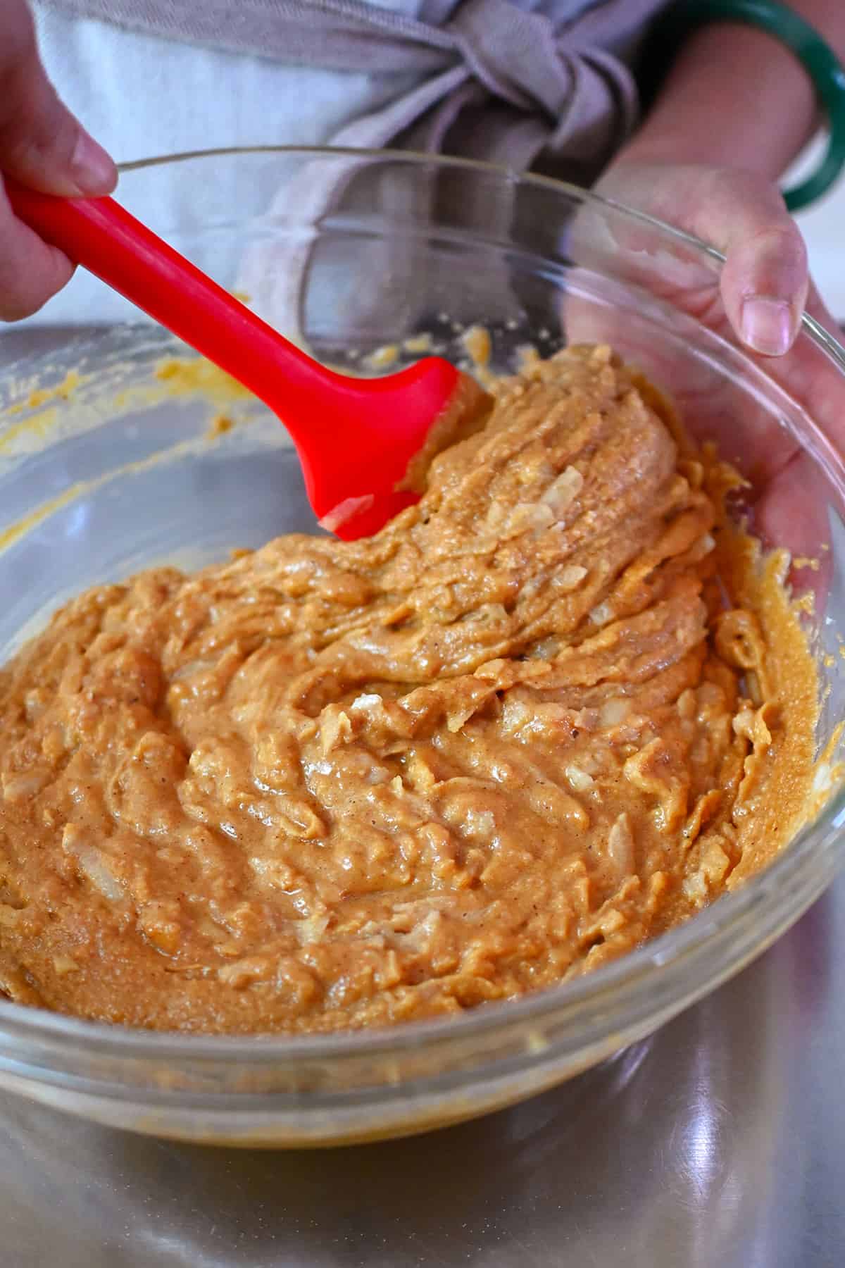 A closeup of the raw paleo apple muffin batter in a large mixing bowl being mixed with a red spatula.