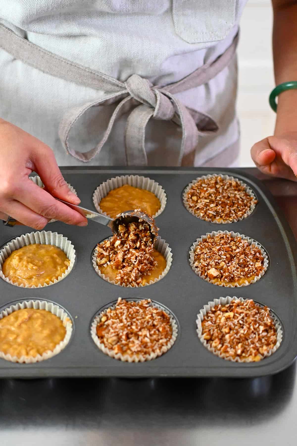 Adding a spoonful of grain-free streusel on top of paleo muffins ready to be baked.