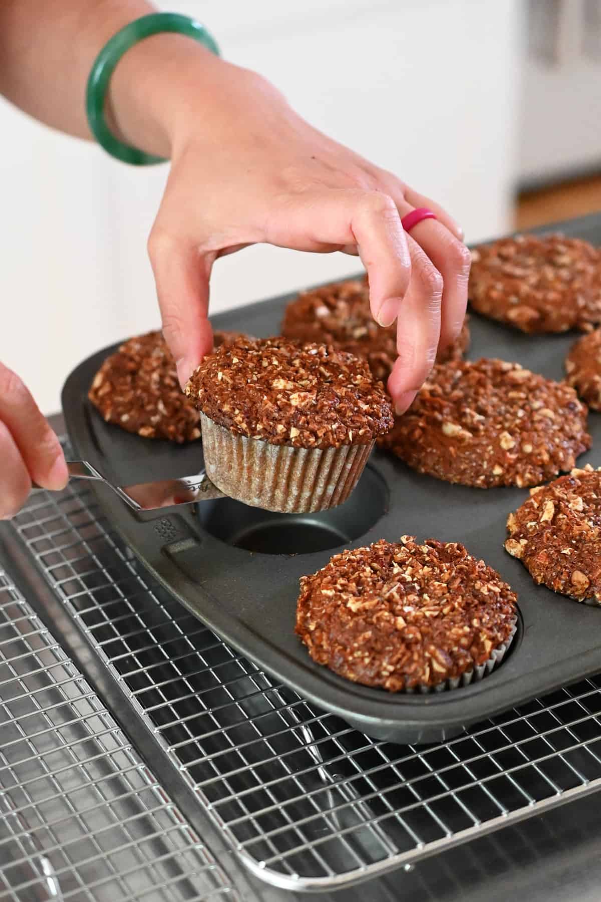Removing the baked apple muffins from the muffin pan with a small offset spatula and transferring them to a wire cooling rack.