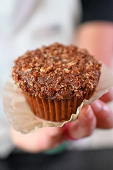 A hand holding a paleo and gluten free apple muffin with the paper liner unwrapped.