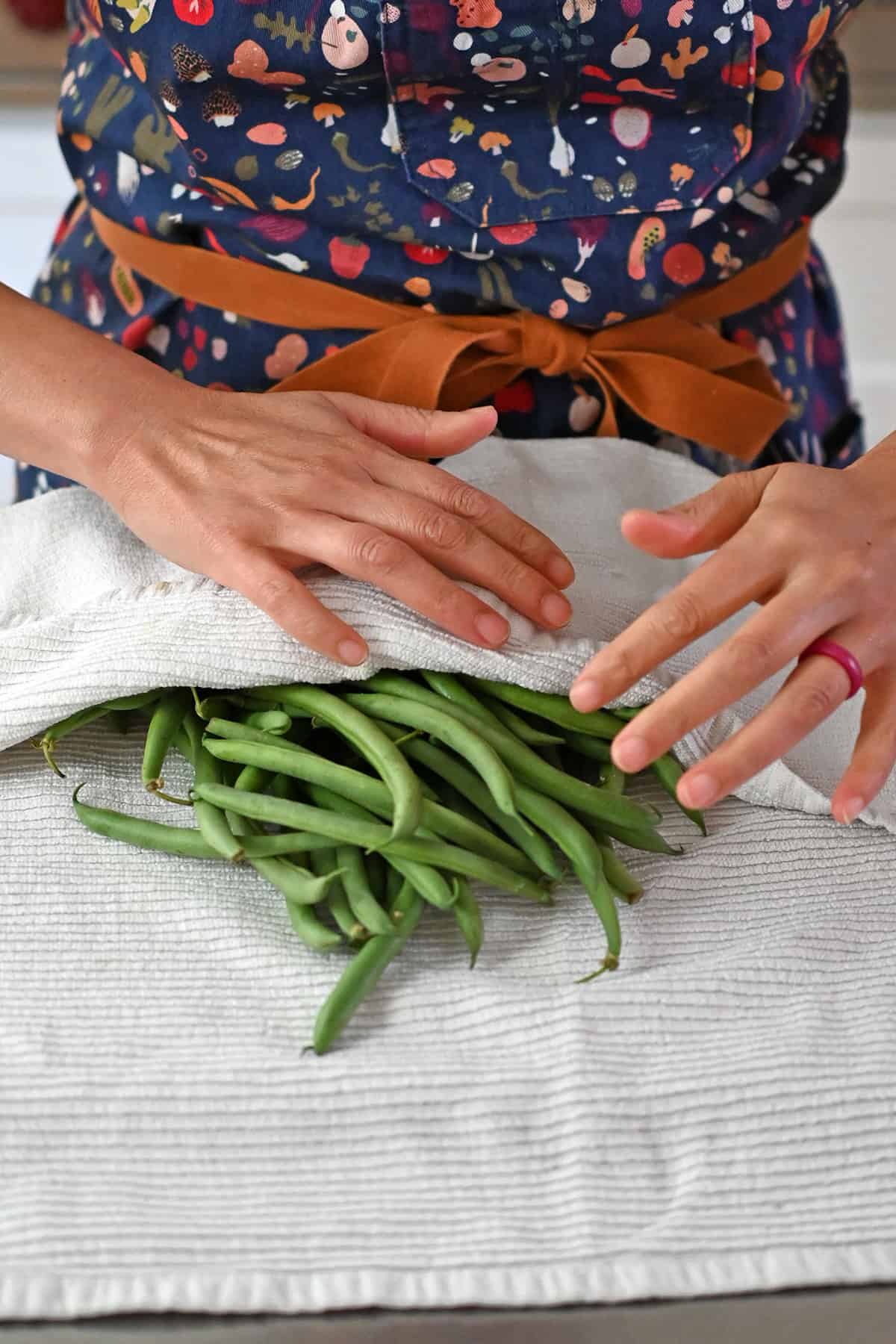 Patting washed raw green beans dry with a clean kitchen towel before cooking them.