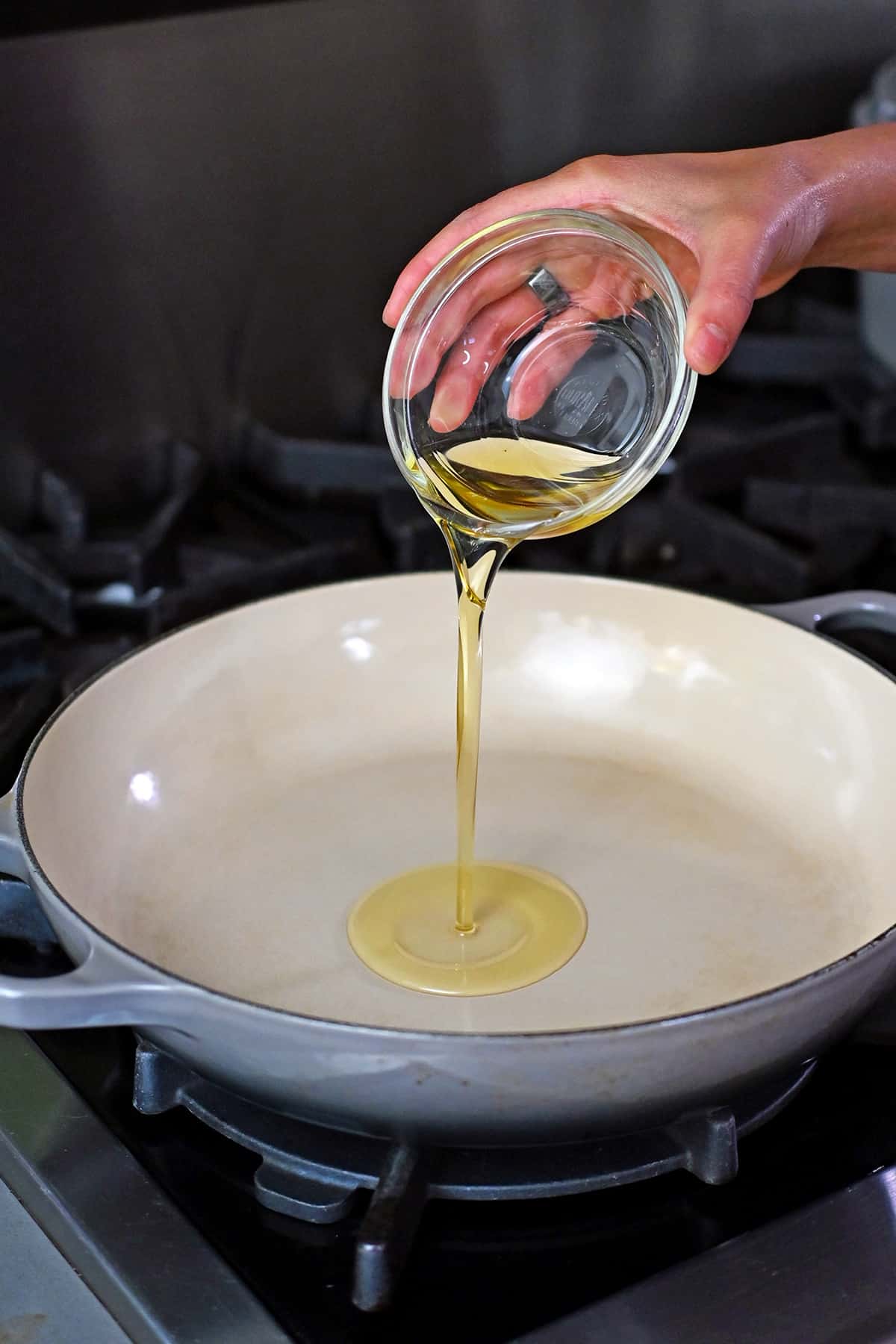 Pouring avocado oil into a large enameled cast iron skillet.