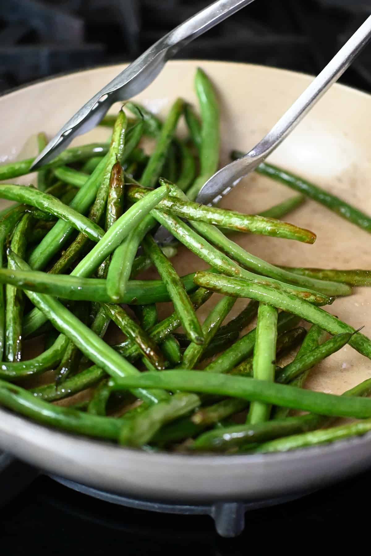 A close-up of the blistered stir-fried green beans in an enameled cast iron skillet.