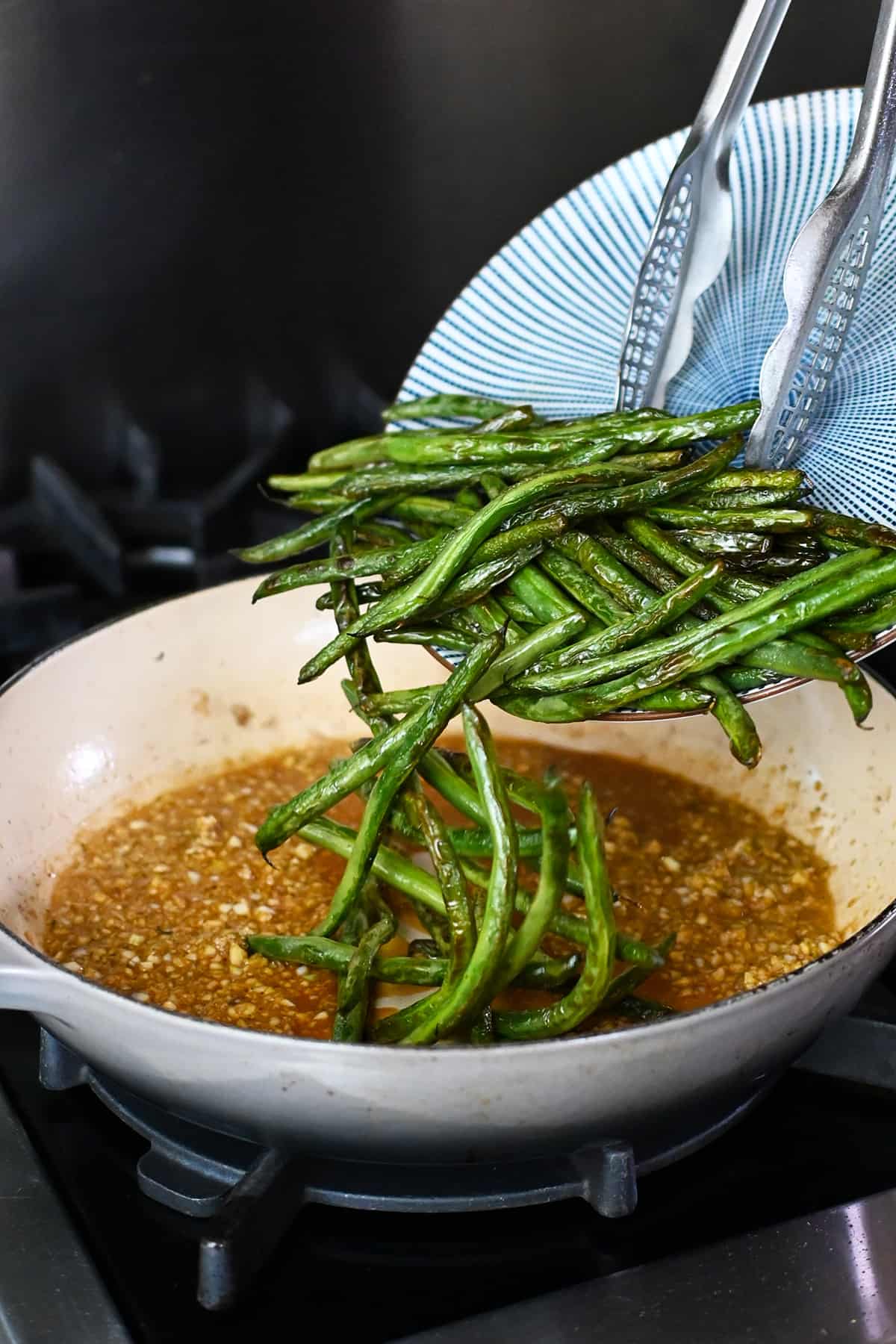 Adding the blistered green beans back into the skillet with the garlic sauce.