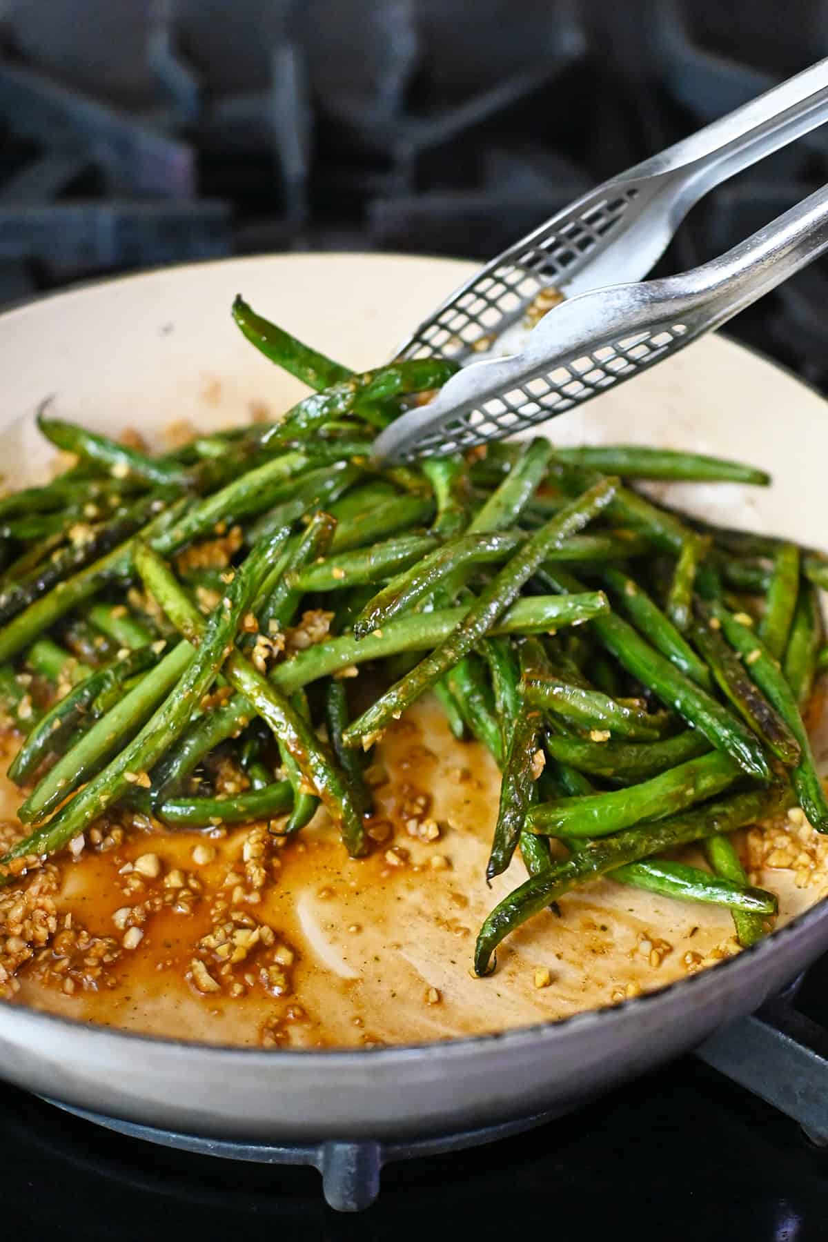 Tossing blistered green beans in a pan with a Chinese garlic sauce.