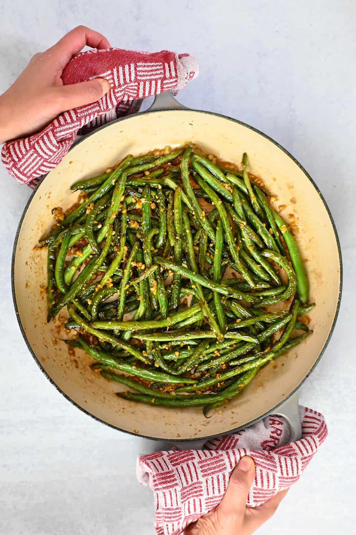 An overhead shot of a enameled cast iron skillet filled with Chinese garlic green beans.