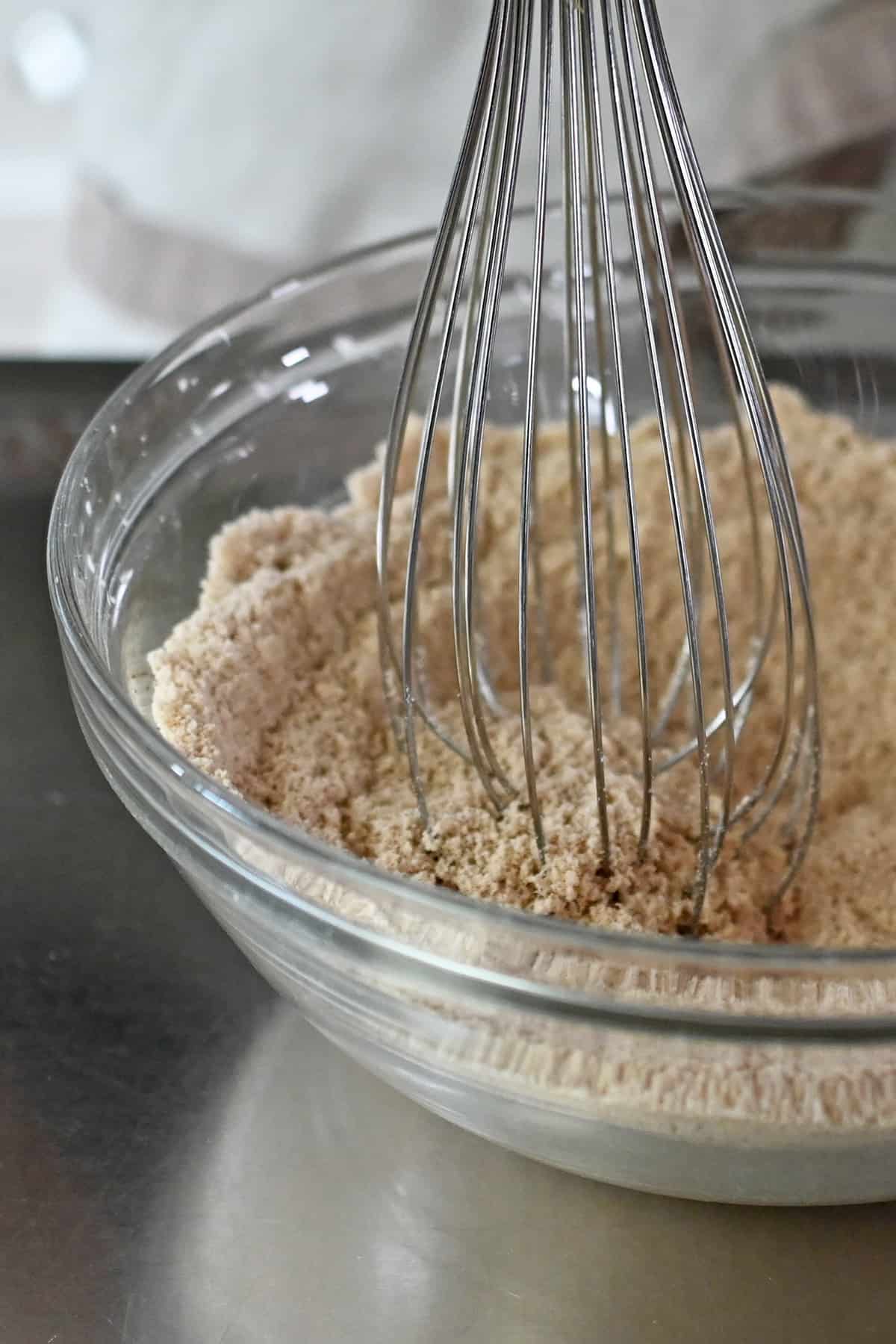 A closeup of a metal balloon whisk mixing the dry ingredients to make paleo pumpkin cookies.