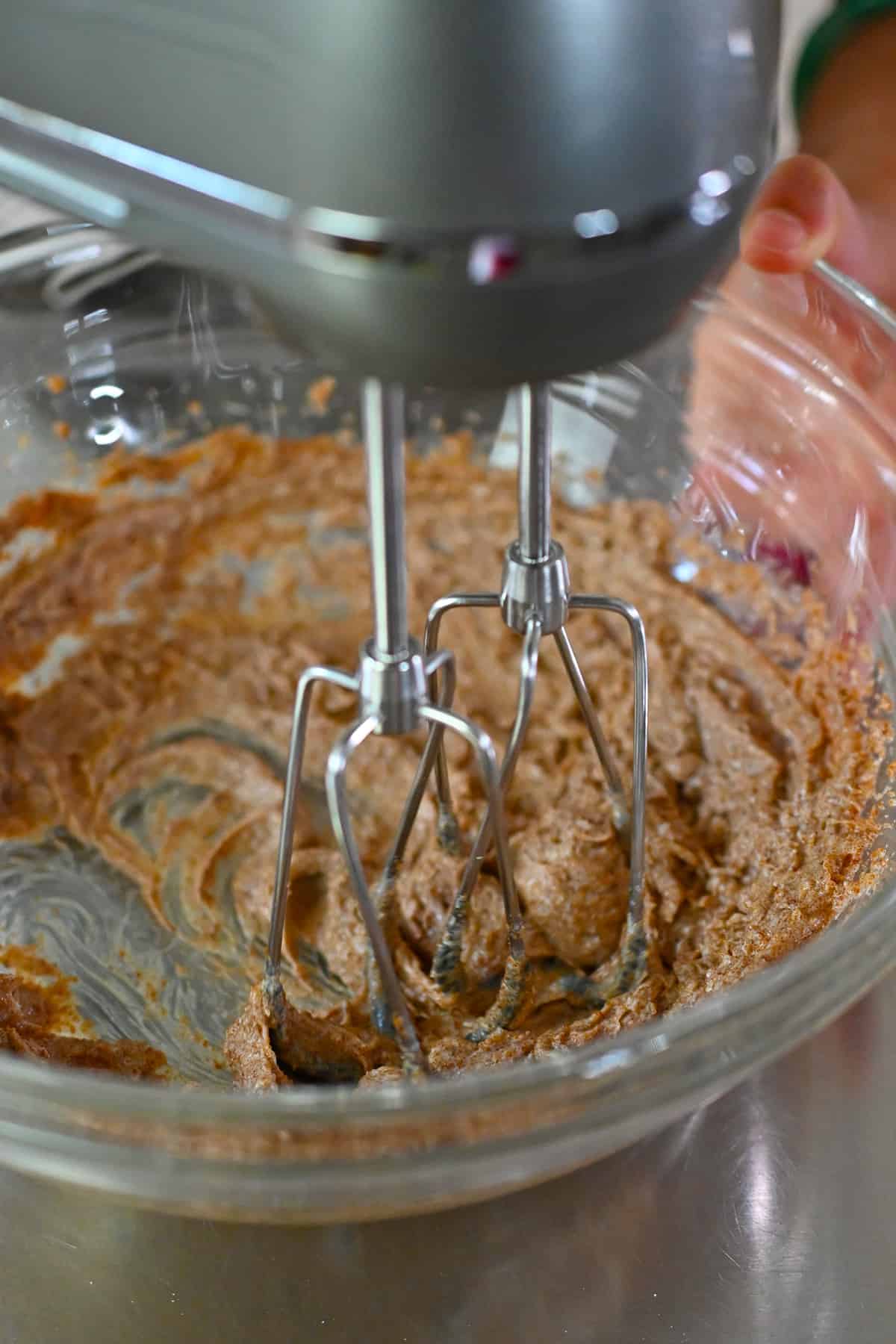 An overhead shot of a hand mixer blending together coconut oil and coconut sugar to make pumpkin cookies.