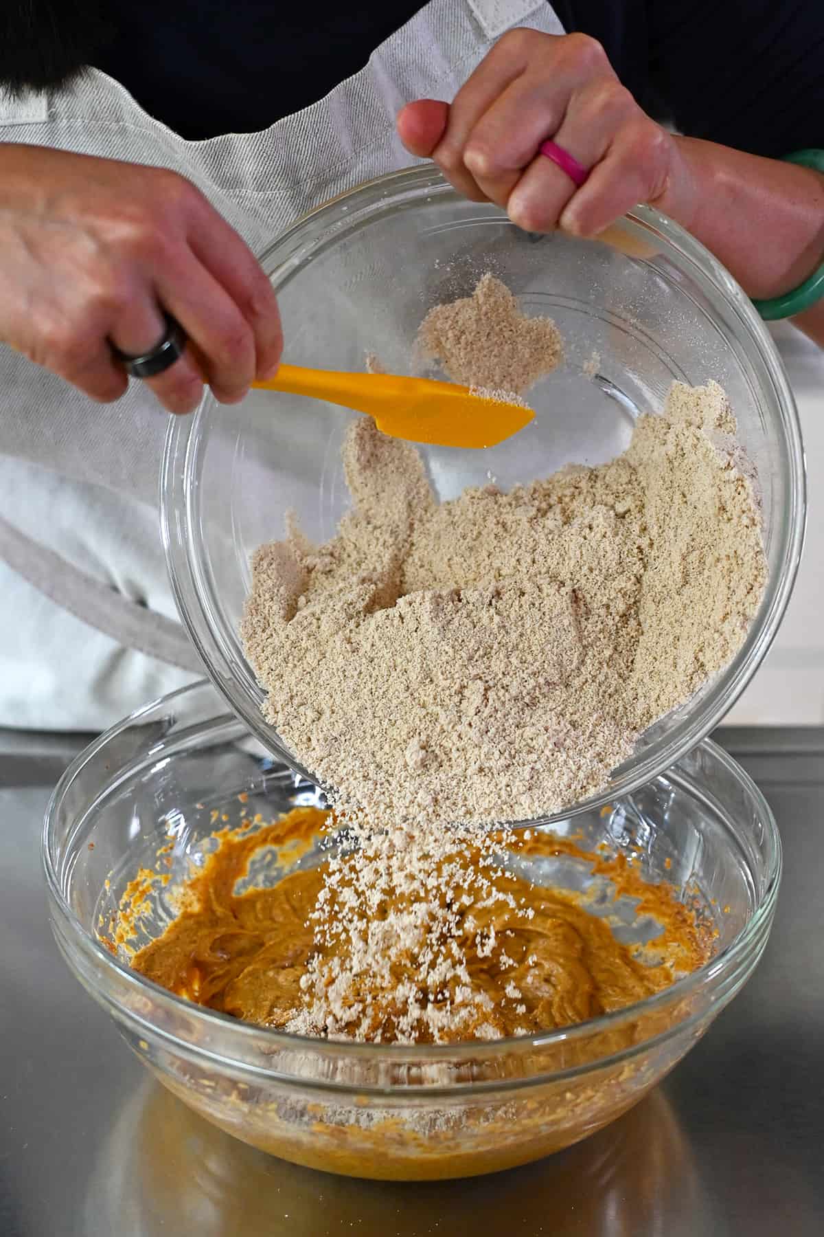 Adding the almond flour mixture to the bowl of wet ingredients to make paleo and gluten free pumpkin cookies.